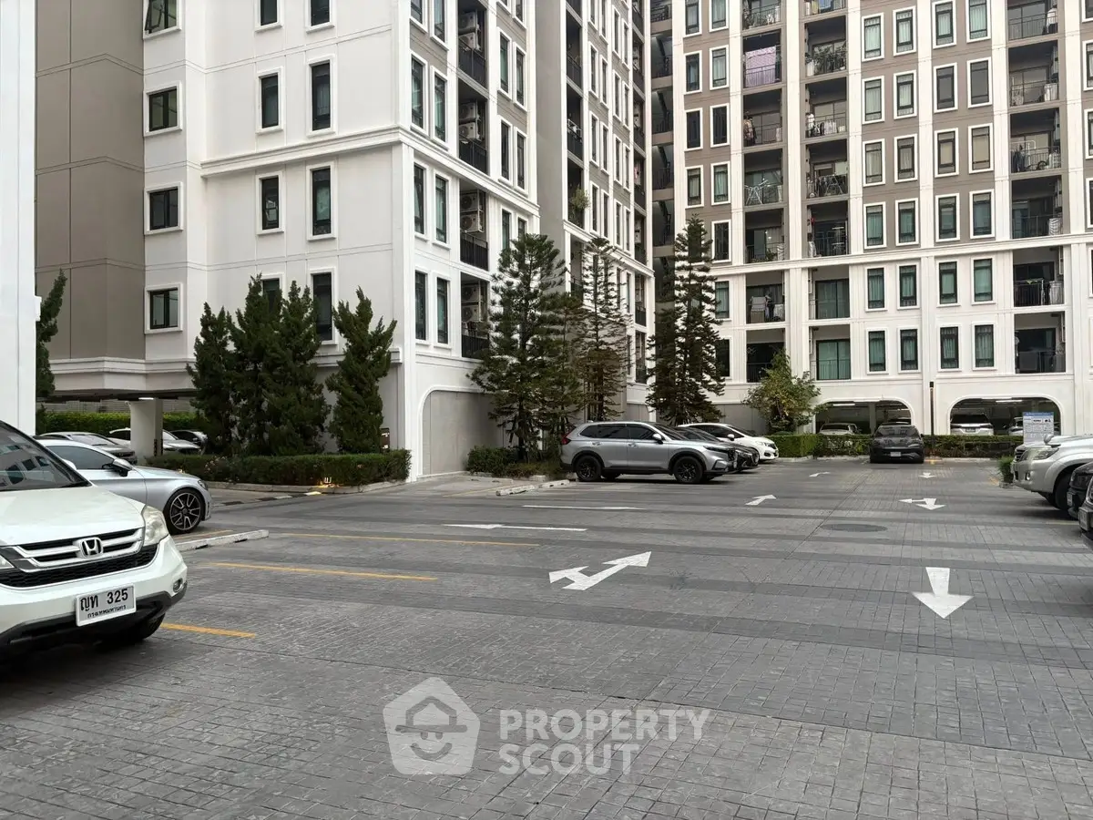 Modern apartment building with spacious parking area and lush greenery.