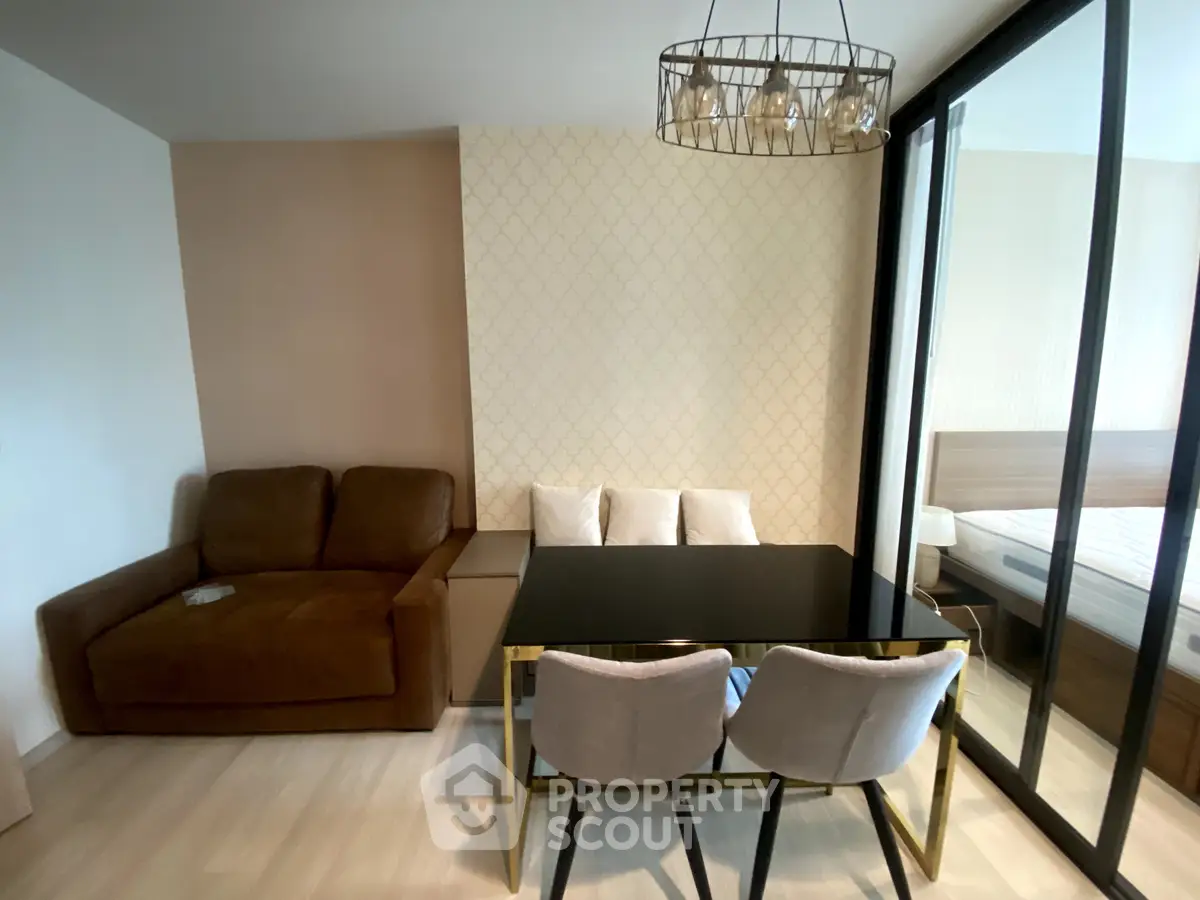 Modern living room with stylish dining area and cozy seating, featuring elegant lighting and a glimpse of the bedroom.