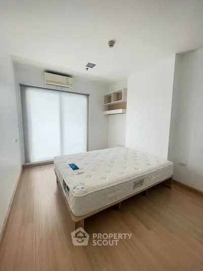 Spacious bedroom with minimalist design and natural light, featuring a comfortable mattress and modern air conditioning.