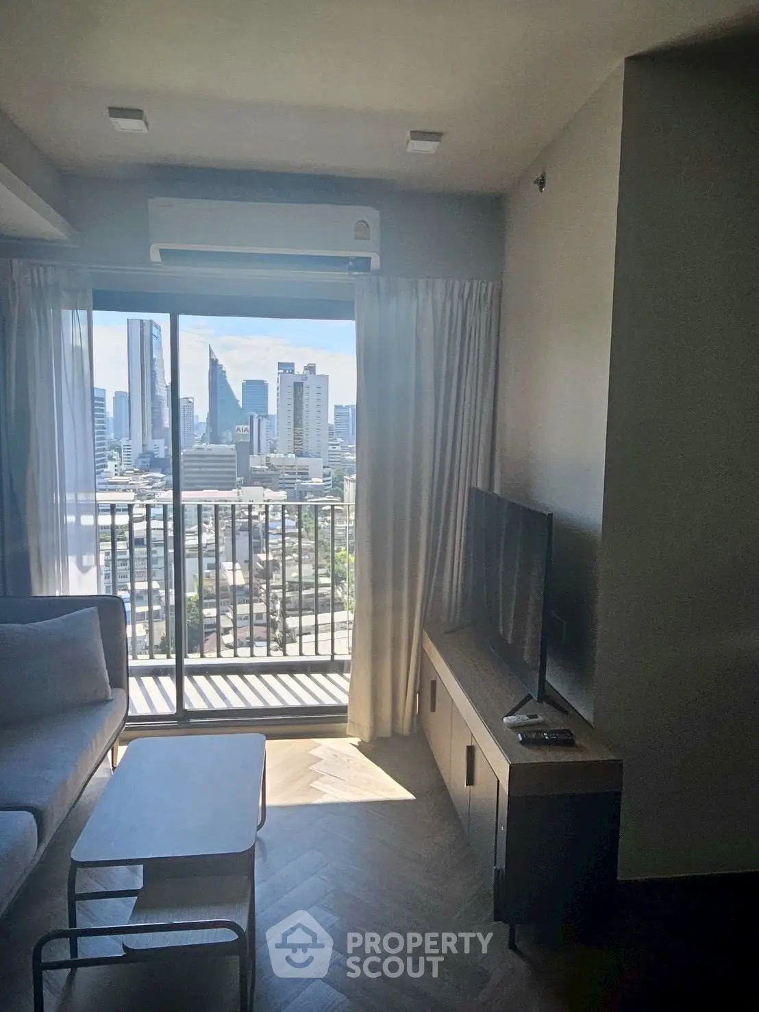 Modern living room with city view and balcony access, featuring sleek furniture and natural light.