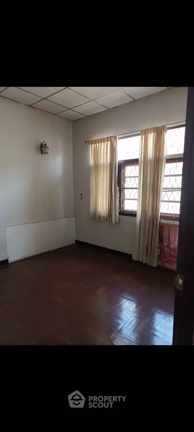 Spacious empty room with wooden flooring and natural light from large windows.