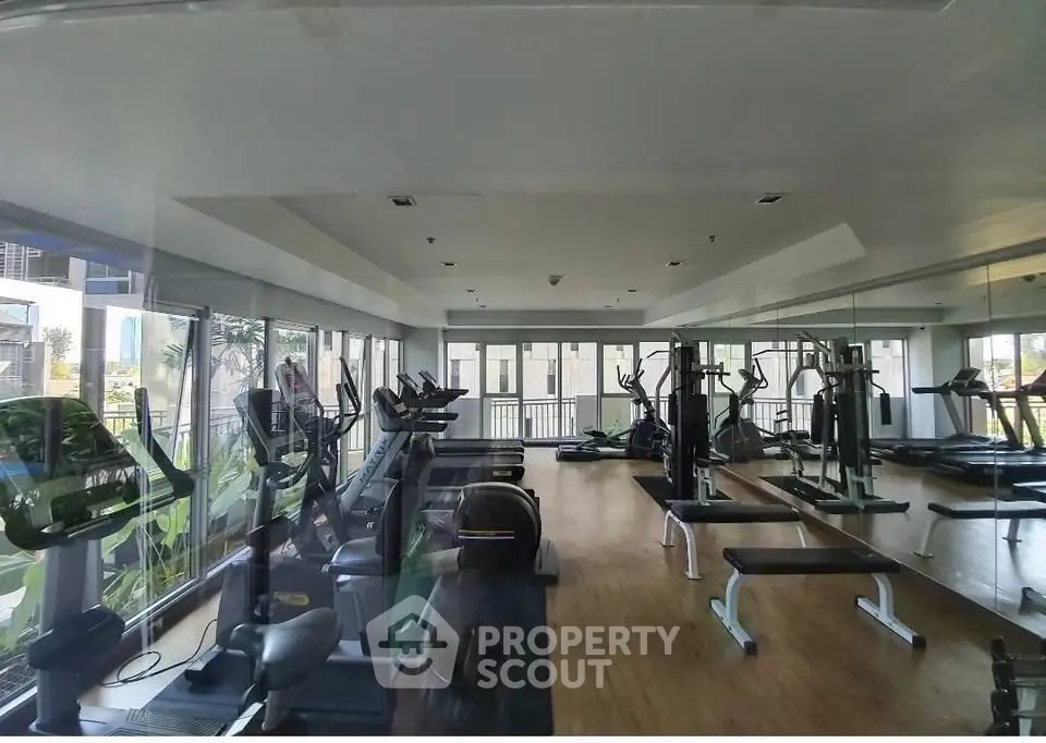 Spacious gym with modern equipment and large windows offering city views.
