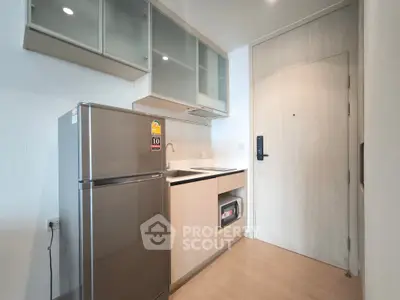 Modern kitchen with sleek cabinetry and stainless steel fridge in compact apartment.
