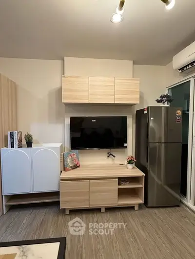Modern living room with sleek furniture and large TV, featuring stylish storage solutions and a stainless steel fridge.