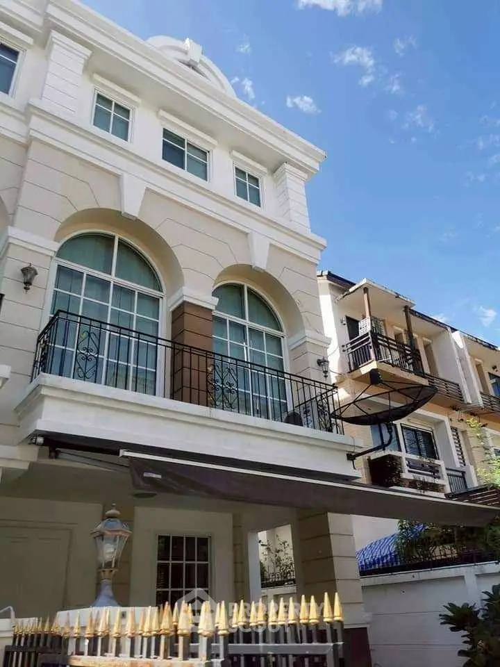 Elegant multi-story townhouse with arched windows and balconies under a clear blue sky.