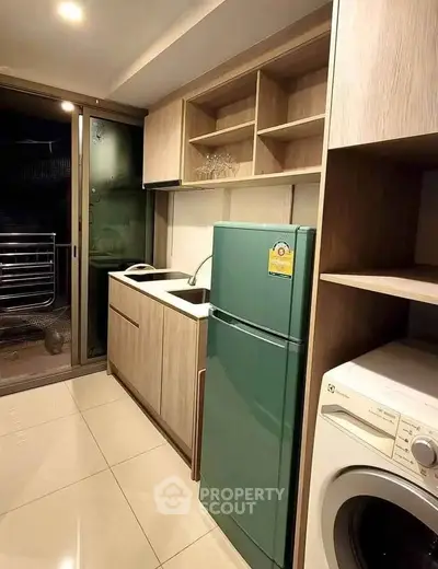 Modern kitchen with green fridge and washing machine, sleek cabinetry, and balcony access.