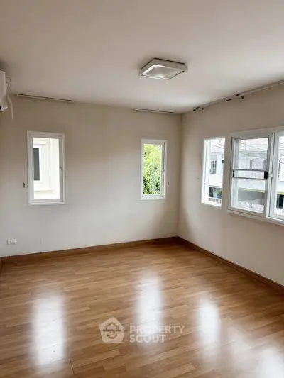 Spacious empty room with wooden flooring and multiple windows for natural light.
