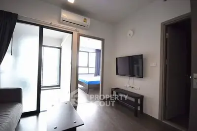 Modern living room with wall-mounted TV and access to bedroom and balcony, featuring sleek design and natural light.
