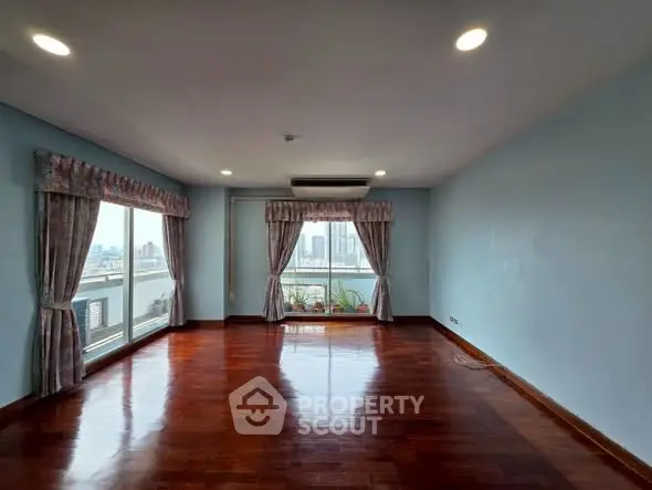 Spacious living room with large windows and city view, featuring elegant curtains and polished wooden floors.