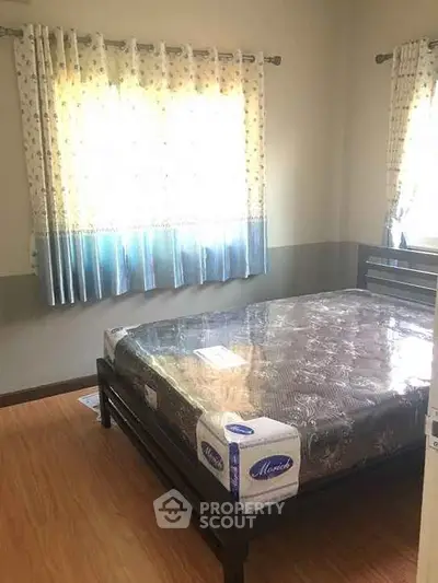 Cozy bedroom with natural light and wooden flooring, featuring a neatly made bed.