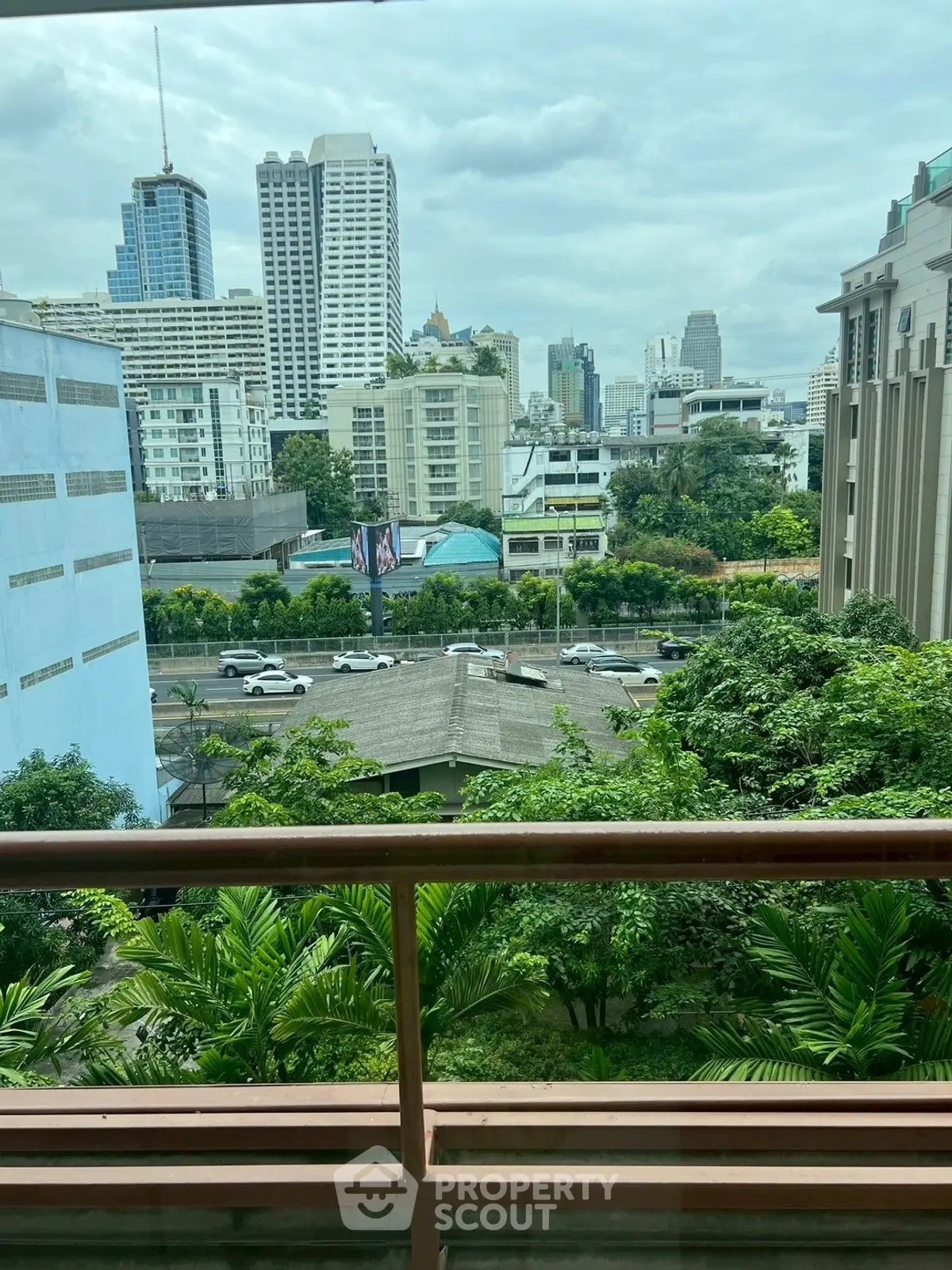 Stunning cityscape view from a balcony overlooking lush greenery and urban skyline.