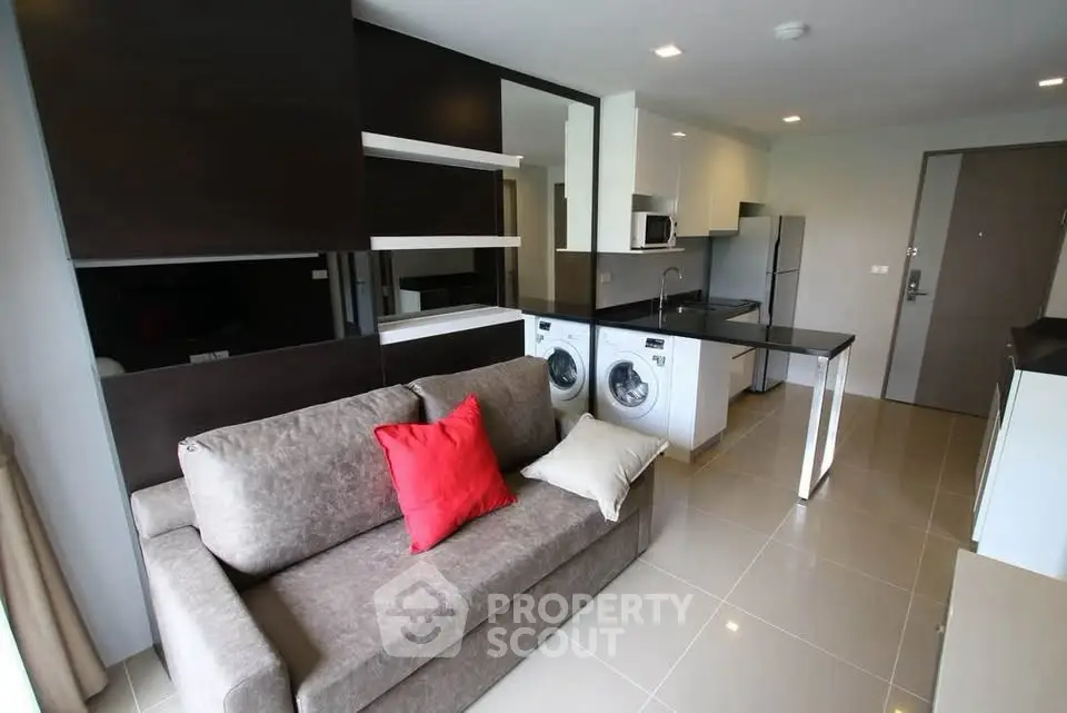 Modern open-plan living room with kitchen and laundry area, featuring sleek appliances and stylish decor.