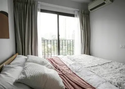 Cozy bedroom with large window and city view, featuring modern decor and air conditioning.