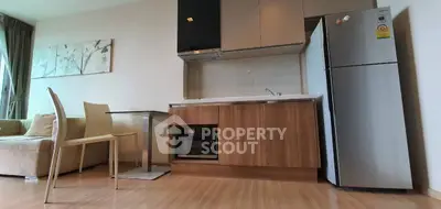 Modern kitchen with sleek cabinetry, stainless steel fridge, and cozy dining area in open-plan apartment.