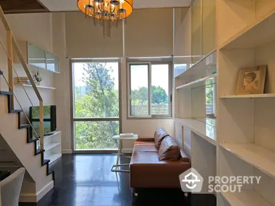 Bright and airy living space with high ceilings, modern staircase, and expansive windows offering a serene view, complemented by elegant shelving and chic lighting fixtures.