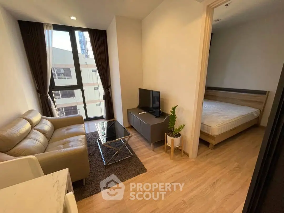 Modern apartment living room with cozy sofa and TV, adjacent to a bedroom with natural light.
