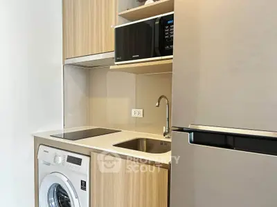 Modern kitchen with sleek appliances including washing machine, microwave, and fridge in compact layout.