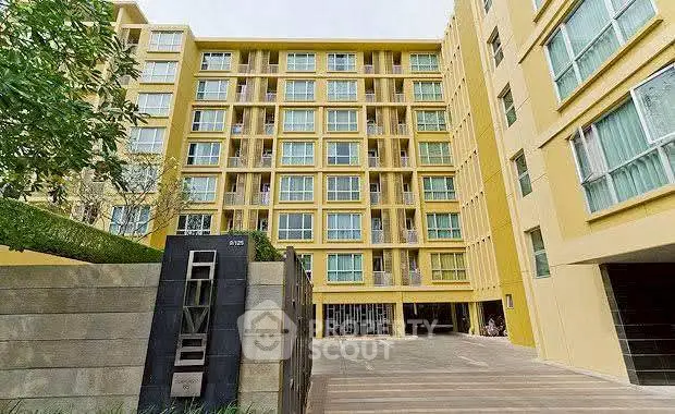Modern yellow apartment building exterior with spacious courtyard and lush greenery.