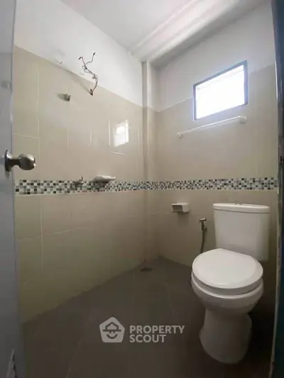 Compact bathroom with tiled walls and small window, featuring a toilet and shower area.
