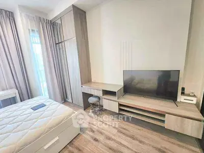 Modern bedroom with stylish furniture and large TV, featuring elegant wood flooring and natural light.