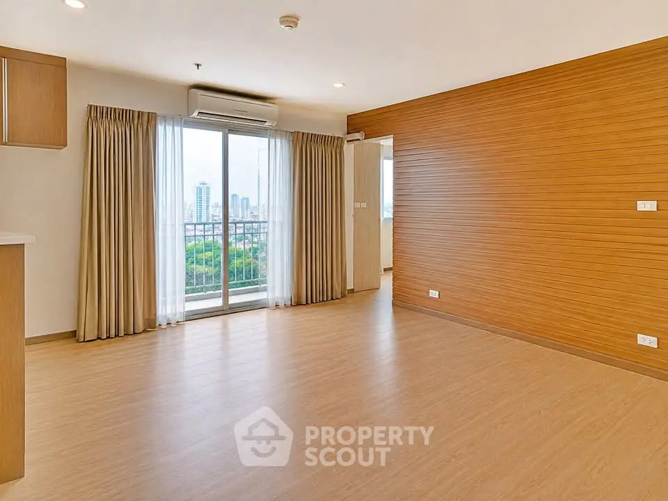 Spacious empty living room with wooden flooring and large window offering city view.