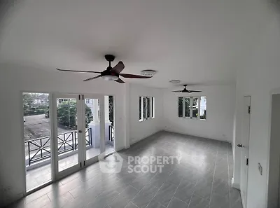 Spacious living room with ceiling fans and large windows opening to a balcony, offering ample natural light.