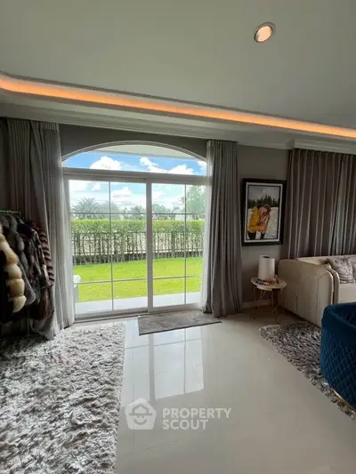 Luxurious living room with large window offering stunning garden view, elegant decor, and plush furnishings.