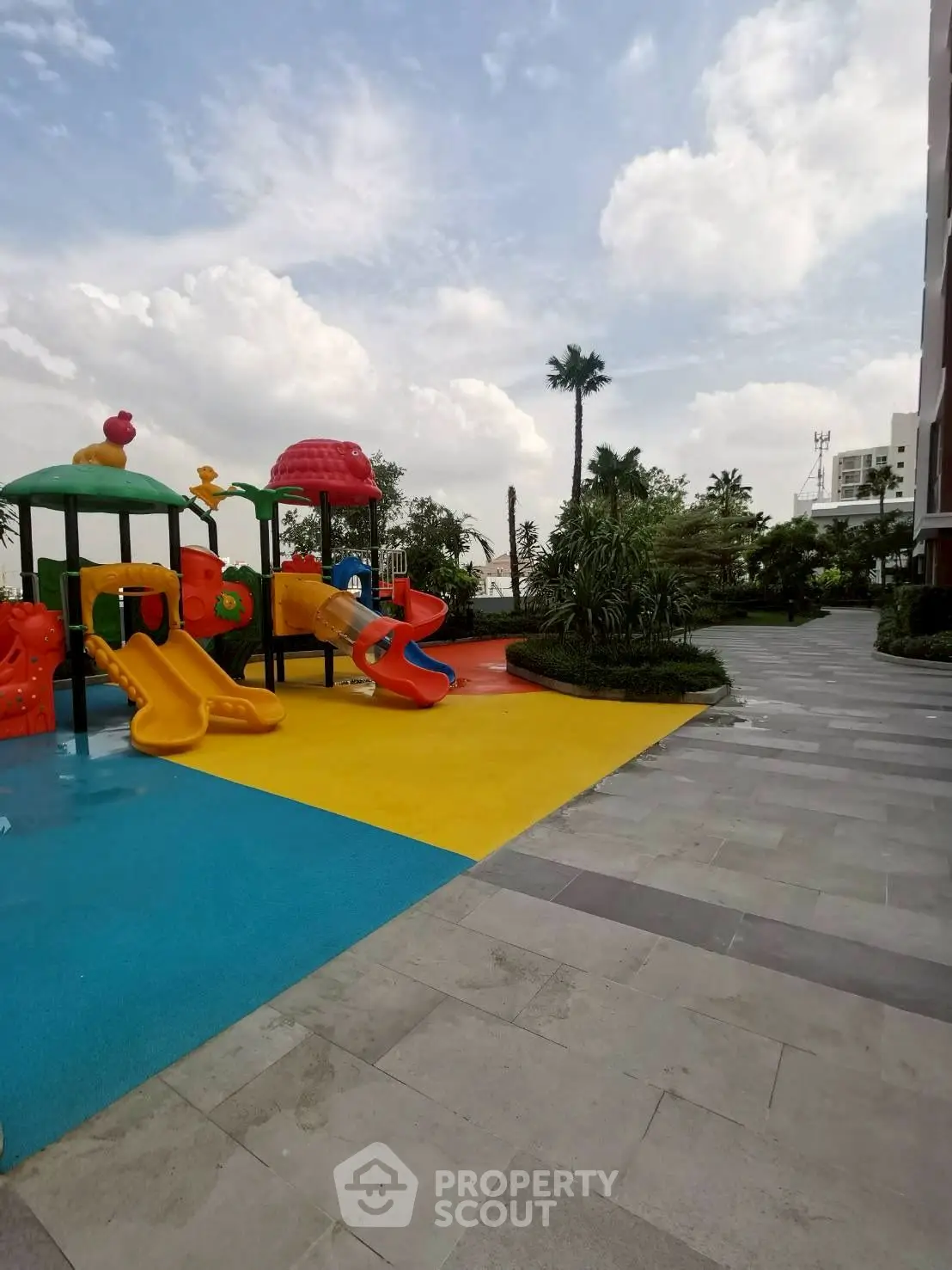 Vibrant playground in modern residential complex with lush greenery and clear skies.