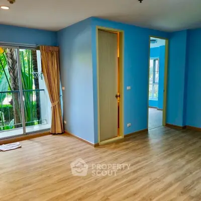 Spacious living room with blue walls and large window overlooking garden, featuring wooden flooring.