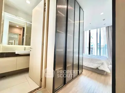 Modern bedroom with glass wardrobe and ensuite bathroom in a stylish apartment.