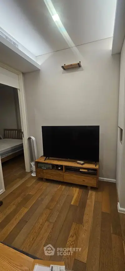Cozy living room with wooden flooring and modern TV setup, adjacent to a bedroom.