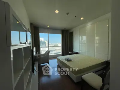 Spacious bedroom with large window offering city view, modern furnishings, and ample natural light.