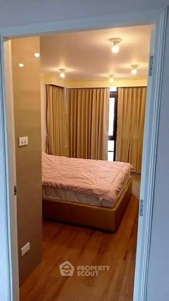 Cozy bedroom with wooden flooring and soft lighting, featuring a comfortable bed and elegant curtains.