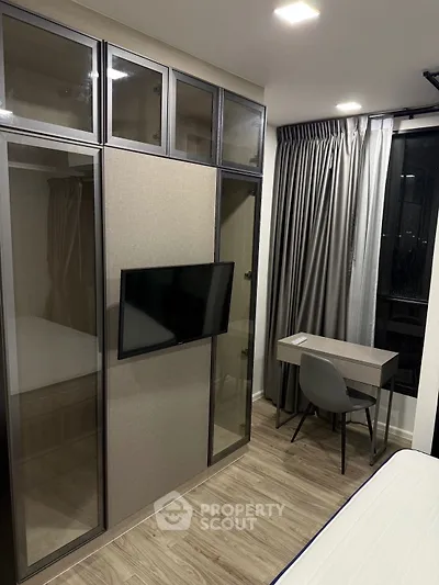 Modern bedroom with sleek wardrobe, wall-mounted TV, and compact study desk.