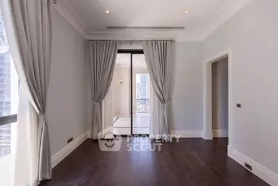 Elegant empty room with hardwood floors and large windows, featuring luxurious curtains and a balcony view.
