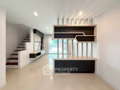 Modern living room with sleek built-in shelving and staircase, featuring contemporary design and ample natural light.