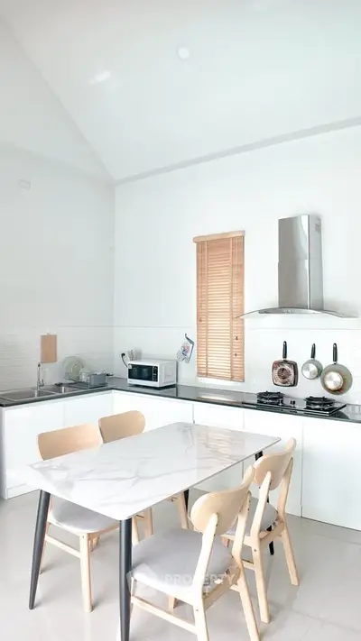 Modern kitchen with sleek white cabinets, gas stove, and dining area with marble table.