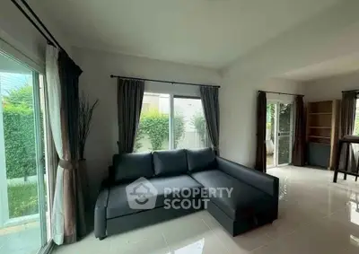 Spacious living room with modern sofa and large windows overlooking lush greenery.