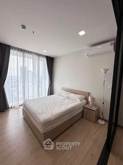 Modern bedroom with large window and wooden flooring in a stylish apartment.