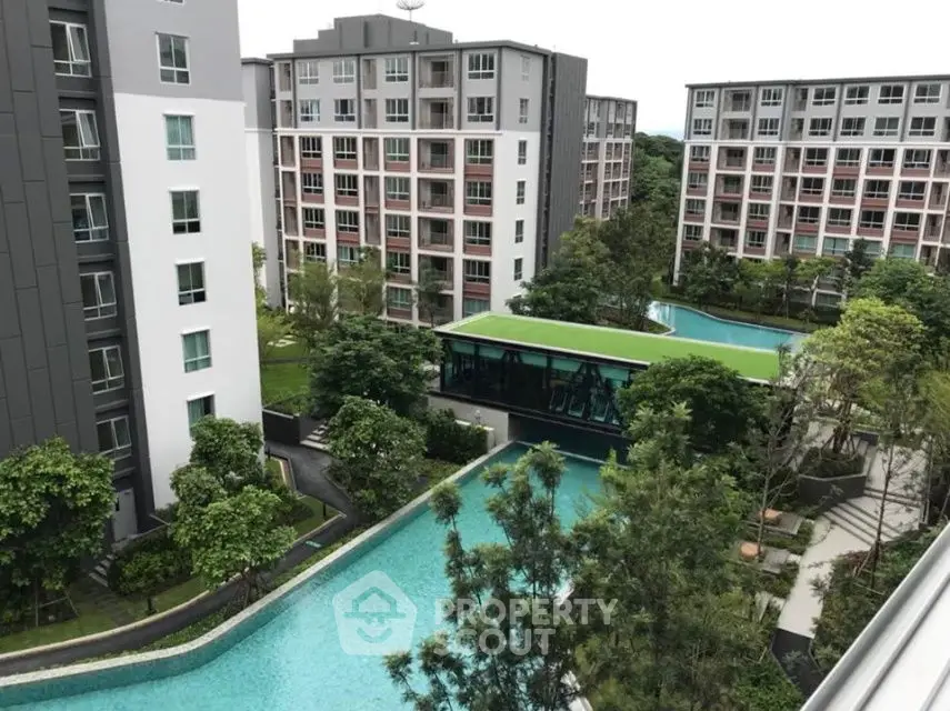 Modern apartment complex with lush gardens and large swimming pool view.