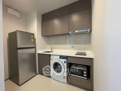 Modern kitchen with sleek appliances including fridge, washing machine, and microwave in compact layout.