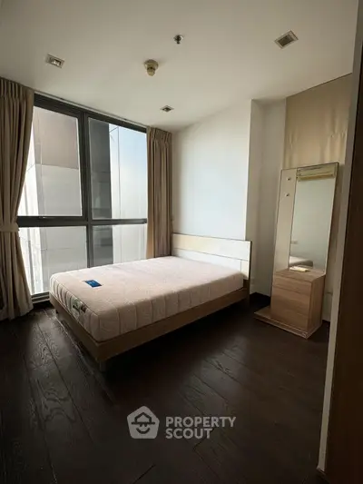 Spacious bedroom with large window and modern furnishings in a high-rise apartment.