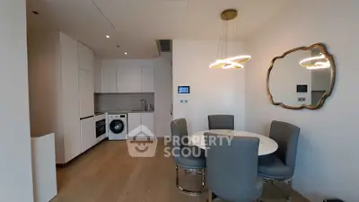 Modern kitchen with dining area, featuring sleek white cabinets, washing machine, and elegant lighting.