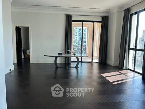 Spacious living room with dark wood flooring and large windows offering city views.