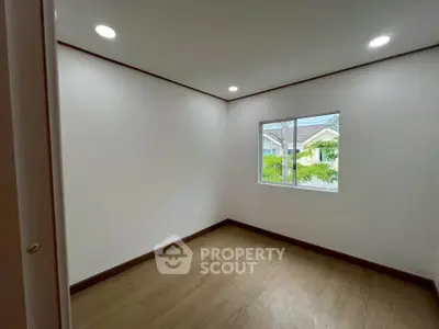 Bright empty room with wooden flooring and window view of suburban houses.