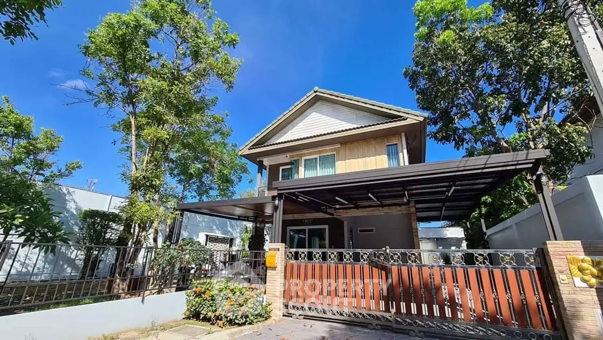Charming two-story house with lush garden and modern carport under clear blue sky.