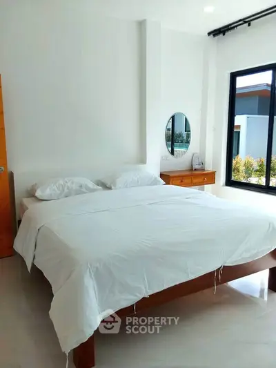 Spacious bedroom with modern decor and large window offering natural light.