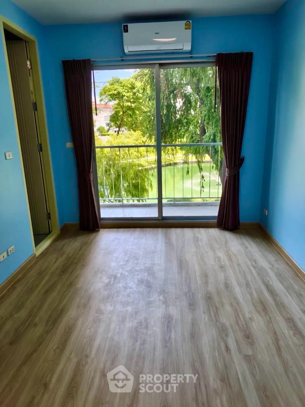 Bright empty room with large window and air conditioning, overlooking lush greenery.