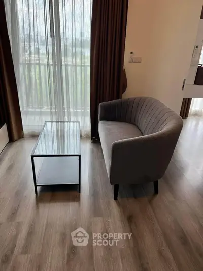 Modern living room with stylish sofa and glass coffee table, featuring elegant wooden flooring and large window.