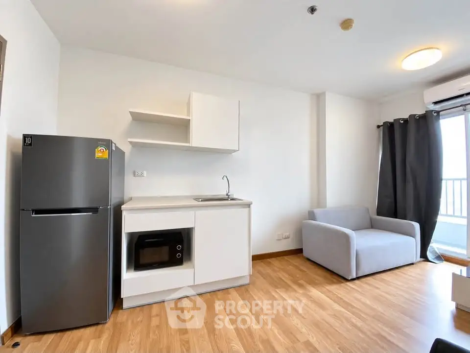 Modern studio apartment with sleek kitchen and cozy living area, featuring a fridge and microwave.